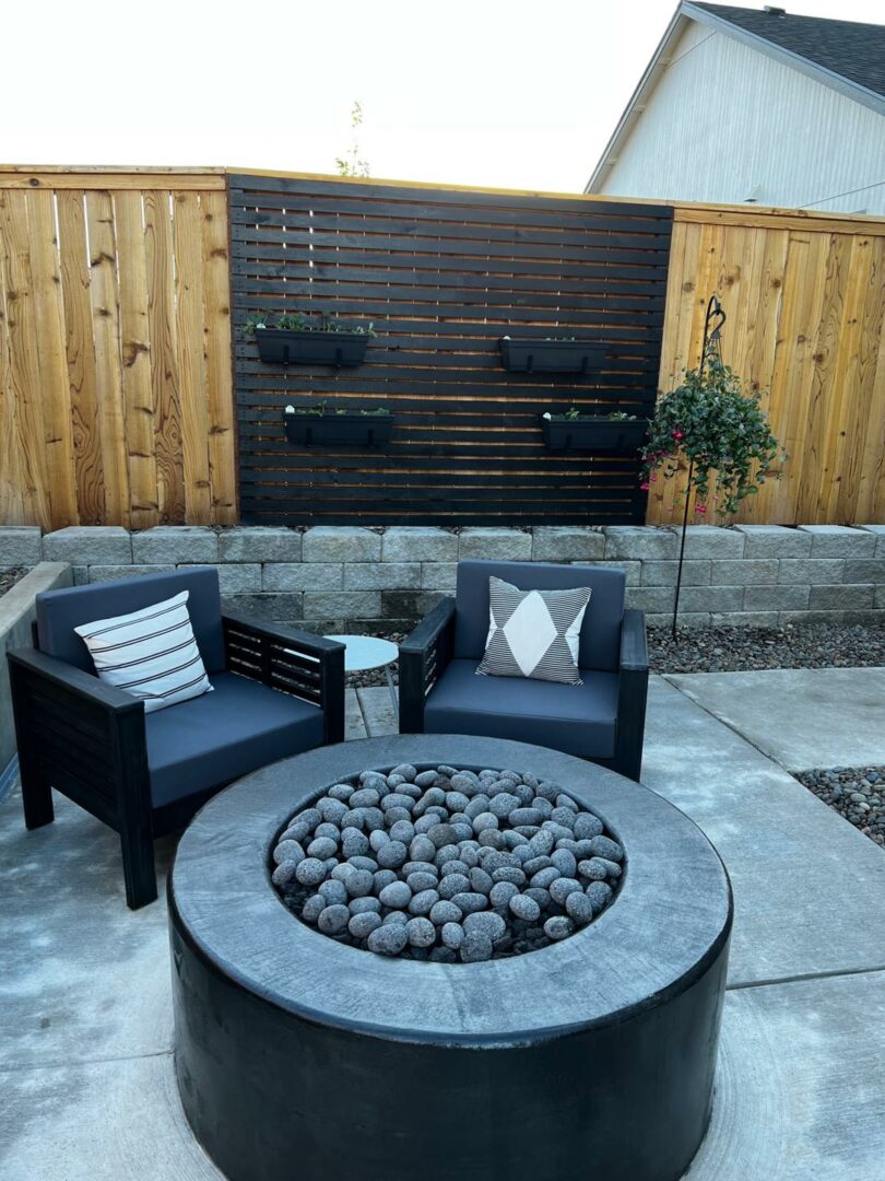 Modern backyard fire pit with chairs and privacy fence, part of an outdoor living space renovation.