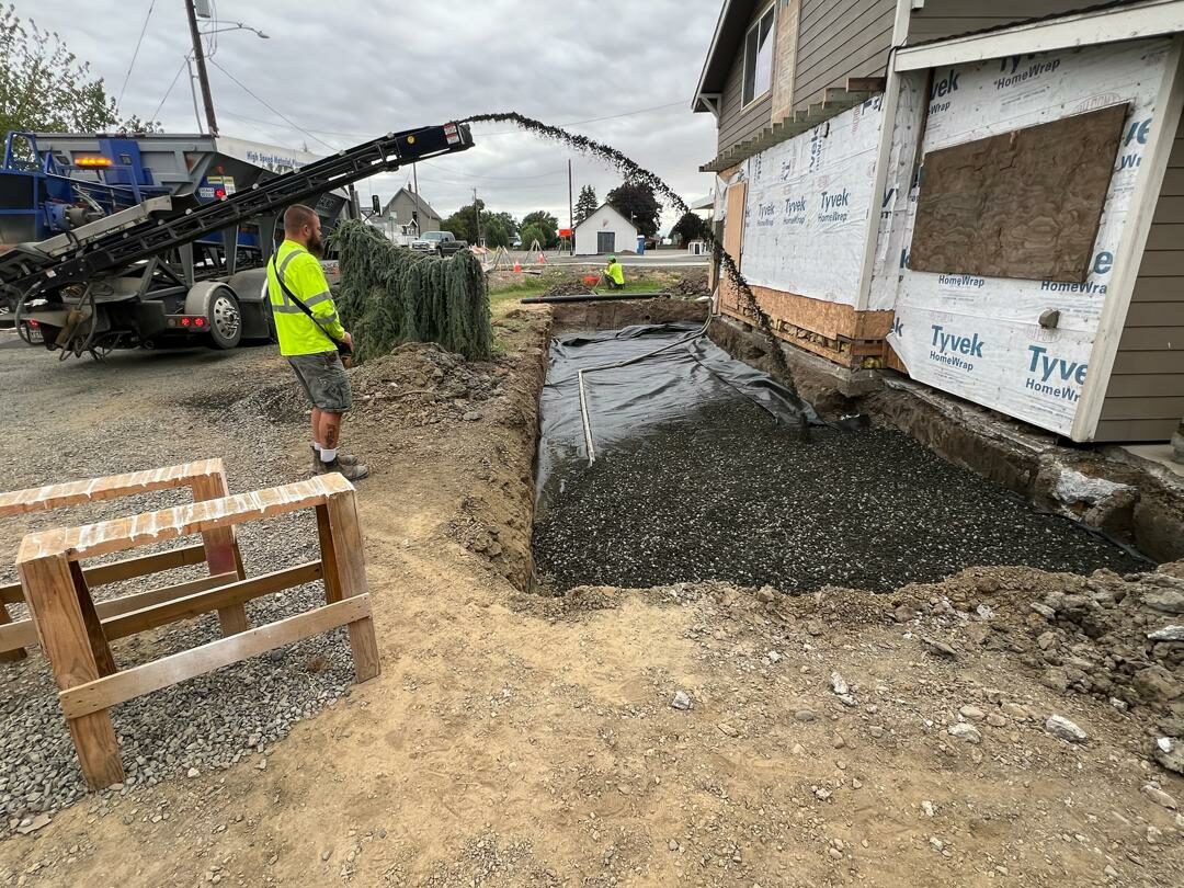 Construction crew placing gravel base for a new foundation and room addition on a residential remodel.